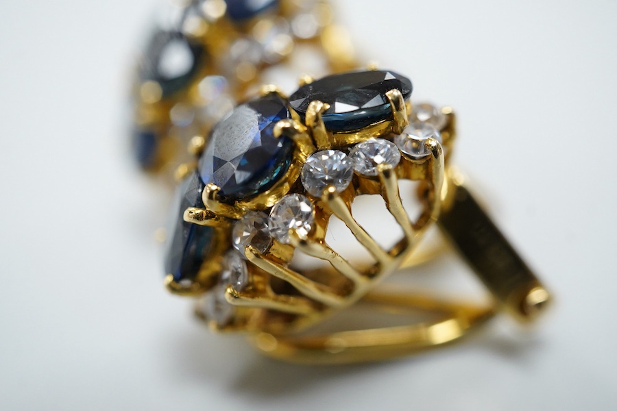 A pair of sapphire earrings, each set with three oval sapphires, within a border of brilliant-cut cubic zirconias, mounted in gold, length 1.4cm each, clip and retractable post fittings